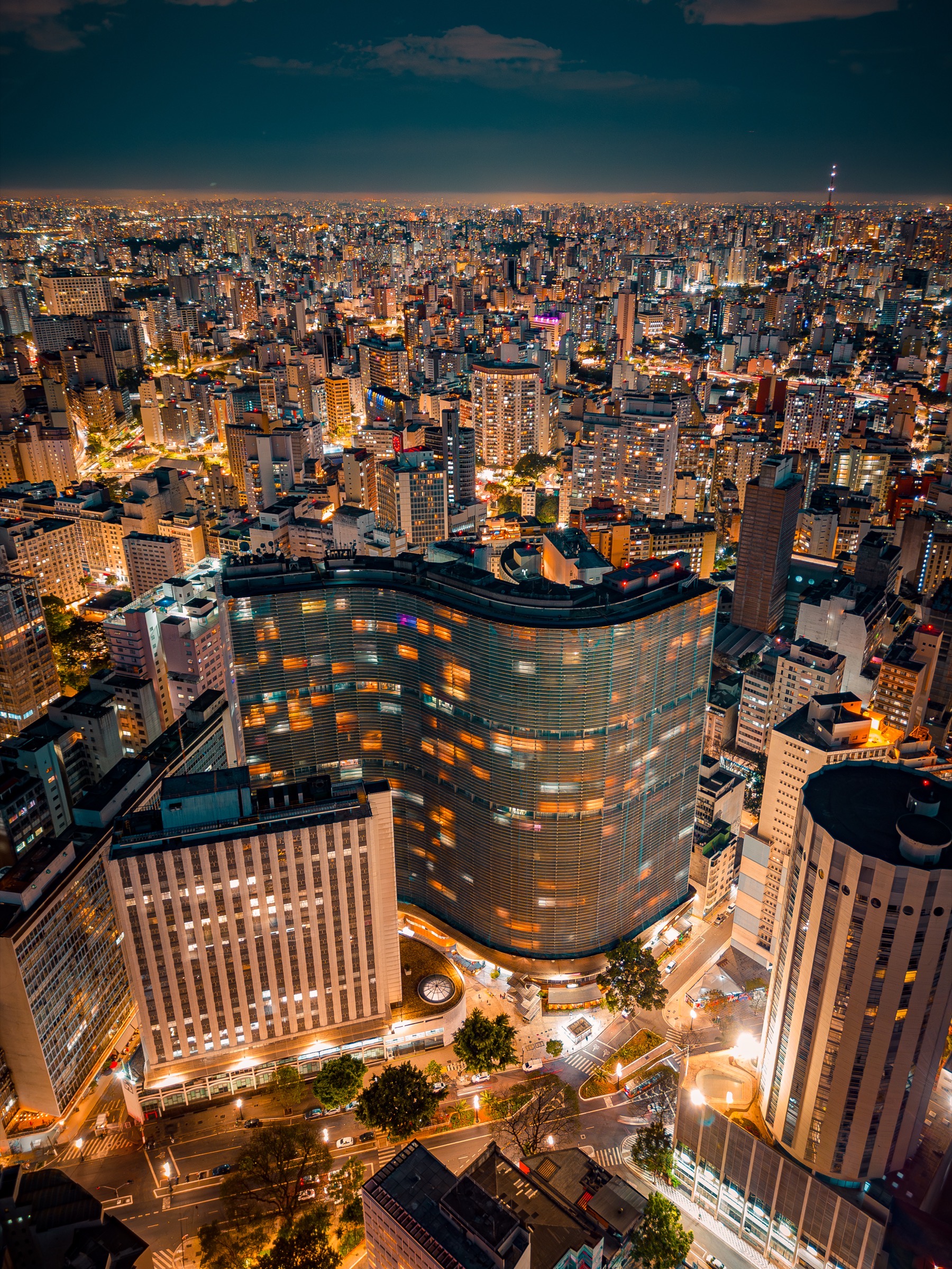 Edifício Copan visto do alto, à noite, com o centro de São Paulo aceso ao redor